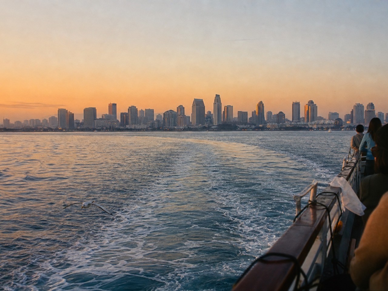 San Diego Bay at dusk from the water, the downtown skyline lit behind a cruise boat wake